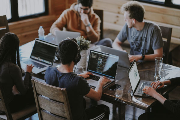 three males on a desk looking at laptops