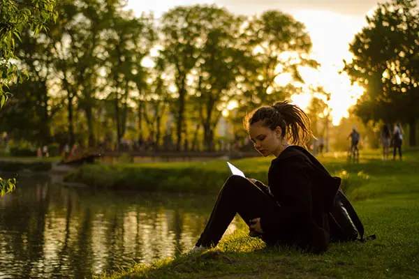 A young woman sits by a lake and reads.