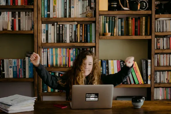 A woman raising her arms in the air behind a laptop.