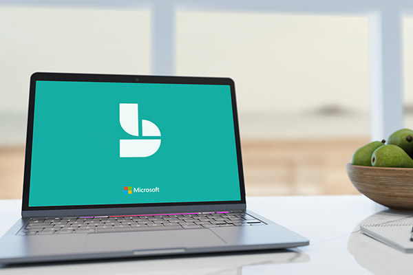 Laptop on a white desk showing the Microsoft Bookings logo, with a bowl of green apples nearby.