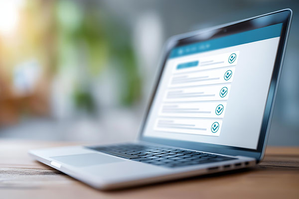 Agos-olwg o liniadur ar ddesg bren yn dangos rhyngwyneb rhestr wirio gyda sawl eitem wedi’u marcio â thiciau gwyrdd. Mae’r cefndir wedi’i niwlio’n feddal gyda golau cynnes a gwyrddni.